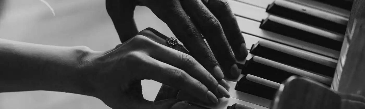Duas mãos tocando piano juntas, em preto e branco