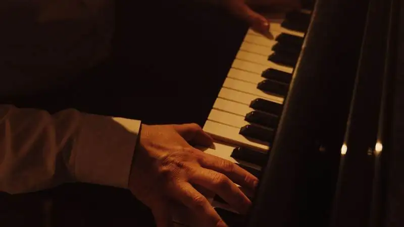 Mãos de um adulto tocando piano, com a manga da camisa social visível, em ambiente com luz quente